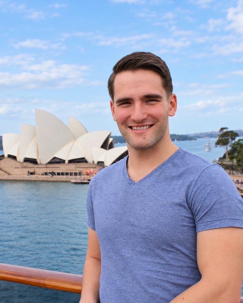 Alex Romano smiling in front of the Sydney Opera House